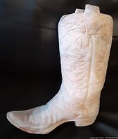 Cowboy boot-shaped flower pot made from plaster or concrete with detailed texture and open shaft for flowers, shown on black background.