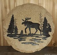 Close-up photo of the circular garden stone wall hanging showing moose and tree motif.