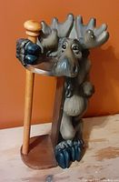 Photo of the wooden moose-shaped paper towel holder with a painted finish, displayed against a plain orange background.