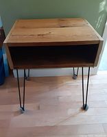 Photo of one wood and metal side table with rectangular wooden top, open shelf below, and black hairpin metal legs with tennis balls on the feet for floor protection.