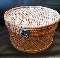 Closed vintage round hat box showing woven wicker exterior and metal clasp on side.