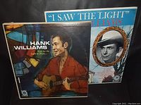 Photo showing two vinyl record albums: Hank Williams 'I Saw the Light' and 'Wait For the Light to Shine', placed side by side for display.