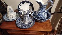 Blue and white floral stoneware pitcher with matching basin, two blue and white plates, and white ceramic pieces stacked on one of the plates.