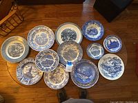 Top-down photo of 12 assorted blue and white decorative plates arranged on a round wooden table