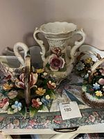 Photo showing four porcelain Capodimonte items including a tall vase with floral decorations and three flower-decorated baskets including a swan-shaped basket.