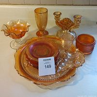 Full view of nine carnival glass items arranged on white surface including plates, bowl, candle holder, glasses, and compote