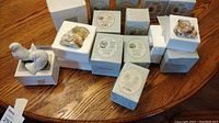 About 10 Cherished Teddies collectibles in their boxes, some showing the teddy bear figurine artwork and original packaging on a wood surface