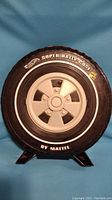 Front side view of closed Hot Wheels Super Rally Case shaped like a black tire with white hub and branding text
