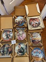 Top view showing 8 colorful 'I Love Lucy' collector plates by Jim Kritz each in individual cardboard protection, some plates partially wrapped in plastic.