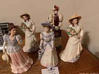 Four lady figurines on wooden surface showing clothing and styling details