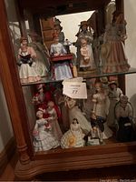 Showcases the full collection of porcelain lady figurines arranged on two shelves inside a glass display cabinet.
