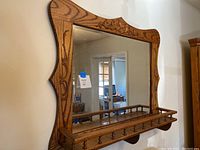 Front view of oak framed mirror with carved floral details and attached shelf with wooden spindles and pegs