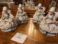 Four porcelain lady figurines in blue and white playing musical instruments set on wooden surface with mirror background