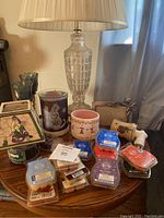 Photo of glass lamp, wax melts, candles, picture frame, and air freshener items on wooden table