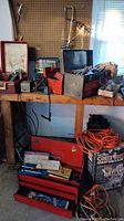 Three rusted metal toolboxes placed on a wooden bench, containing various tools and accessories, with coiled extension cords and boxed shop vacuum below the bench