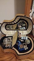 Open piano-shaped jewelry box showing interior fabric lining, mirror, and scattered assorted jewelry pieces