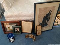 Seven framed pictures with one decorative item arranged on floor; various sizes and wood frames visible