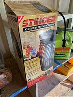 Boxed Stinger Outdoor Insect Control bug zapper shown on a shelf from an angle. Box features branding, product image, and usage details.