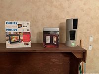 Photo showing box of Philips digital photo frame, box of Seth Thomas clock, and Lasko table fan on wooden surface