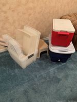 Stack of plastic totes holding lids and next to them a beige stepstool and the two coolers stacked on each other.