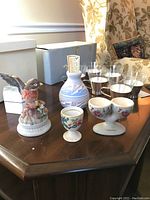 Photo showing egg cups, glass tea cups, blue and white vase, bird figurine on wooden table