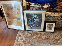 Three framed floral art prints leaning on couch, showing sunflower prints and a white and blue flower bouquet.