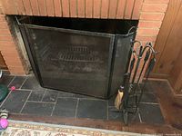 Fireplace with black three-panel screen in front, and black metal fireplace tool stand with four tools to the right side.