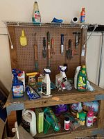 Workbench and pegboard with small garden tools hanging, bottles and containers of fertilizers, pesticides, cleaning and care products on table and shelf below