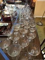 Overall display of the glassware including several dozen stemmed glasses and a tall etched vase