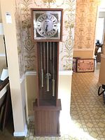 Image of Bentley grandmother clock showing front face, pendulum, chains, and weights inside tall wood case.