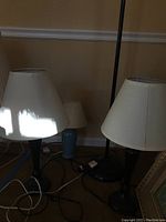Two black table lamps with white shades, a small blue table lamp, and a black floor lamp with white shade grouped together with cords visible