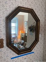Full view of octagonal shaped mirror showing carved wood frame with gold-toned details and mirror reflecting room interior.