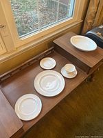 Full view of the eight piece Royal Doulton china set arranged on wooden surface near window, showing the various sized plates, cup, and saucer.