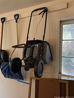 Wide view of fertilizer spreader hanging on wall along with blue snow shovel and other shovels in background