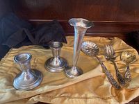 Photo showing the two sterling silver candlesticks, the tall slender vase, serving fork, spoon, and small decorative dish all laid out on a yellow cloth.