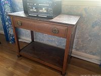 Full view of the vintage wooden table showing its overall structure, drawer with brass pulls, and bottom shelf