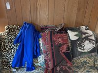 Four folded throw blankets on a floral patterned couch against a wood-paneled wall. Visible leopard print, solid blue, horse themed and wolf themed blankets.