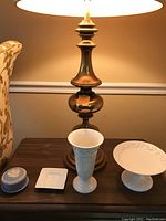 Four Wedgwood ceramic pieces displayed on a table including a small round covered box, square dish, tall vase, and pedestal plate.