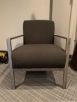 Front-facing view of the dark grey upholstered armchair with metallic legs and arms showing its overall design and fabric texture.