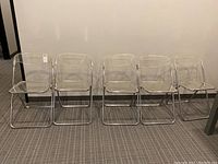 Five clear plastic metal framed folding chairs side by side.