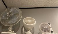 Photo showing three white fans mounted on shelf against white wall and ceiling background.