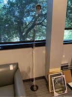Full view of lamp next to window showing black circular base, white support rods, pivot joint and spherical head