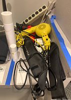Photo showing multiple hair dryers and heat curlers tangled with cords on a surface near power strips.