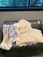 Lot of linens and blankets including Vintage Grocers Supply cruise throw, cream woven throws, MyPillow, metal bin on couch.