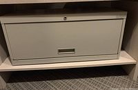 Closed metal file cabinet drawer with lock and recessed handle, light gray finish.