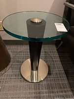 Front view of the modern round glass top side table showing the glass top and black wood conical pedestal with circular metal base.