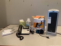 Photo showing items on a table: Lasko heater, AT&T phone with display and handset, Timex digital alarm clock, multiple extension cords, and box for phone system.