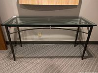 Front view of entry table showing metal frame and clear glass top against a wall with carpeted floor.