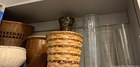 Shelf with four clear glass cylinder vases, amber glass mosaic vase, brown pottery vase, and several woven baskets.