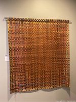 Front view of woven painted canvas wall art hanging on wall with acrylic hanging bar.